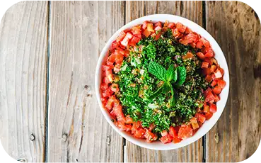 Tabouli salad with fresh Italian parsley, diced tomatoes, onions, bulgur wheat, lemon juice, and olive oil, served in a white bowl.