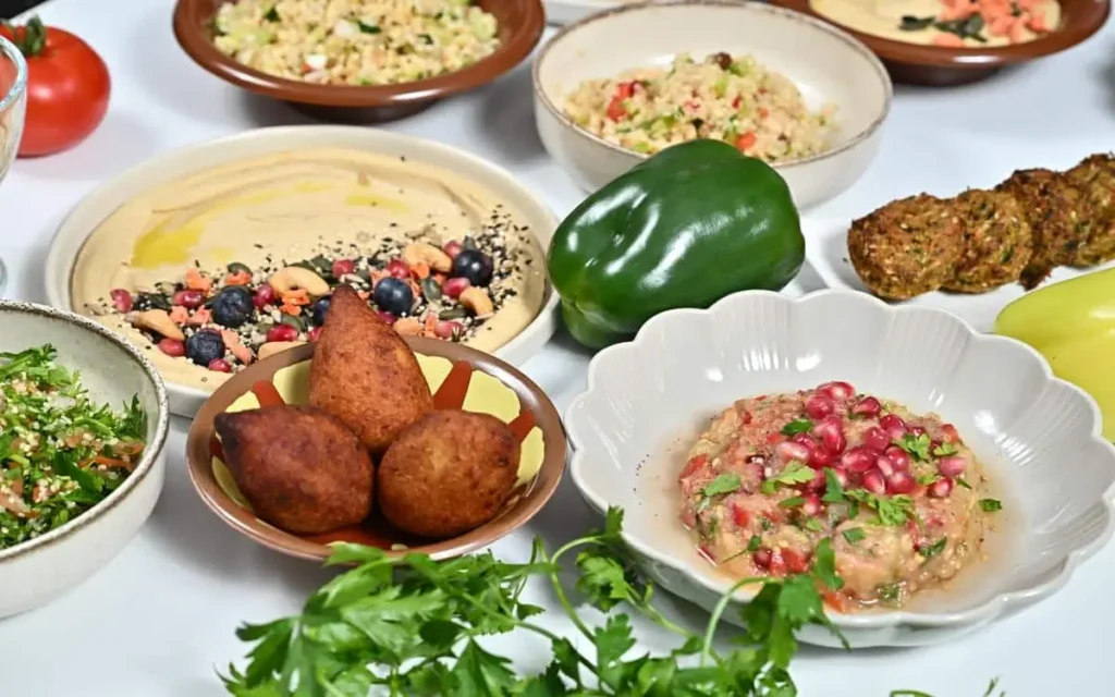 Close-up of kibbeh, creamy hummus with fruit and nut toppings, tabbouleh, and pomegranate dip on a table showcasing appetizers for a Mediterranean catering houston.